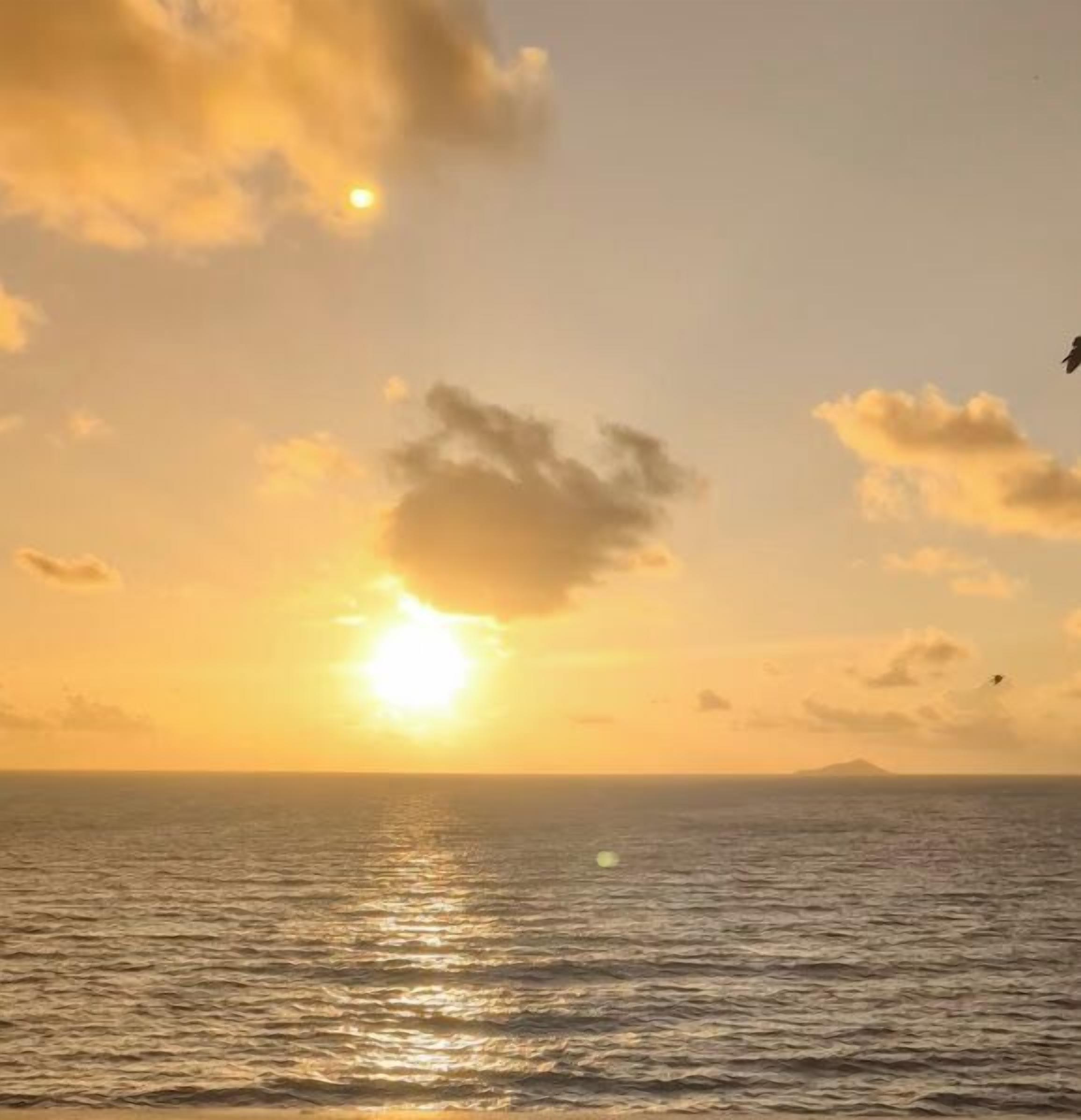 A sunset over a calm sea with a distant landmass.