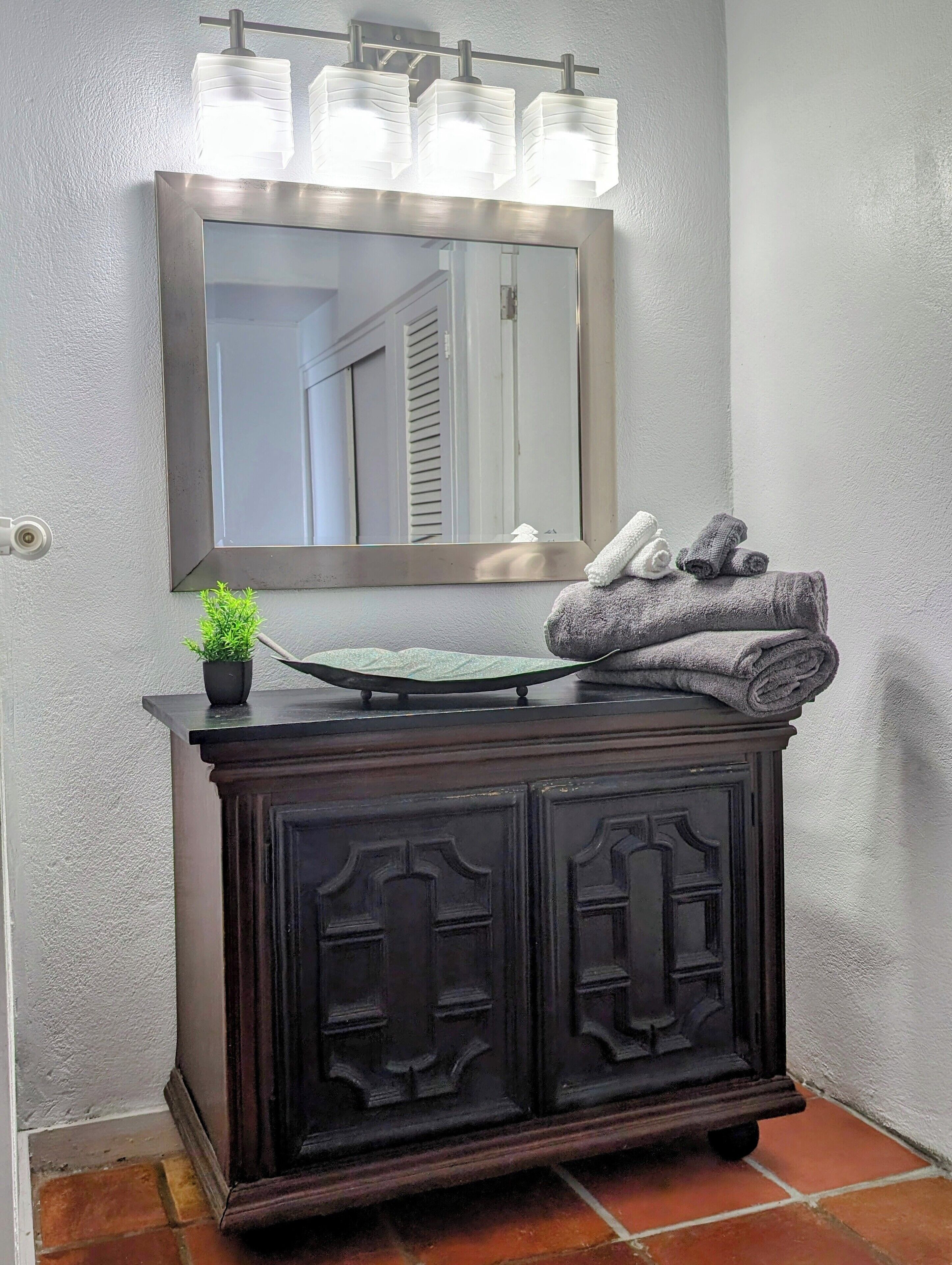 Une coiffeuse en bois foncé, avec un miroir au-dessus, une petite plante en pot et une serviette posée sur le dessus.