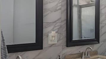 Een badkamer met twee wastafels, donkere marmeren wanden en moderne verlichtingsarmaturen boven de spiegels.