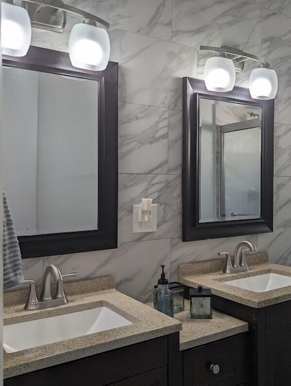 Un baño con dos lavamanos, paredes de mármol oscuro e iluminación moderna sobre los espejos.