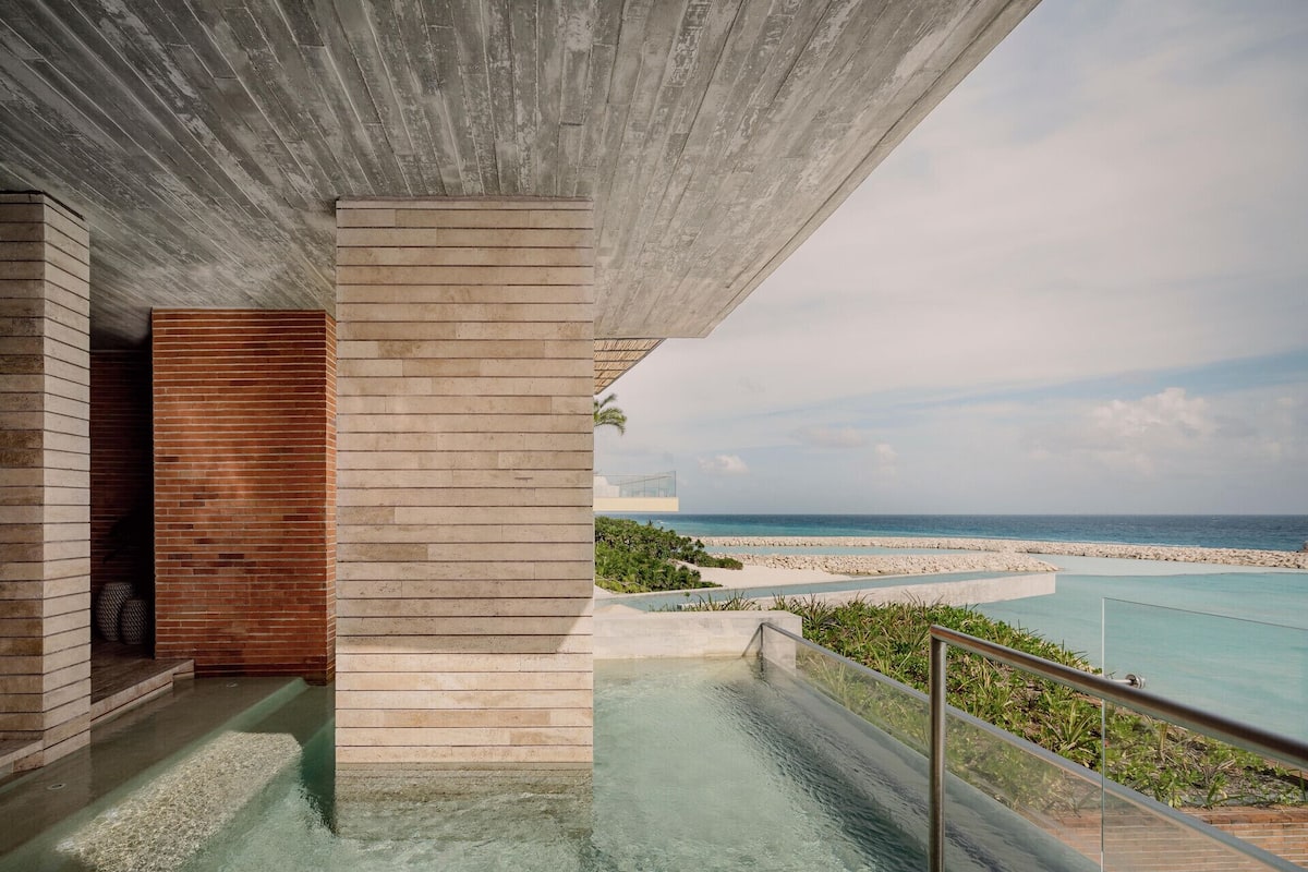 Ein modernes architektonisches Design mit Betondecke, Holztür und Glasgeländer mit Blick auf Strand und Poolbereich.