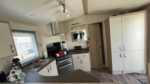 Eine kompakte Küche mit Herd, Backofen, Mikrowelle und Spüle. Ein Fenster mit Jalousien, ein Deckenventilator und ein Schrank mit einer Mikrowelle darauf.