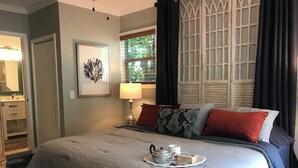 Uma cama bem arrumada com uma bandeja de chá e biscoitos, uma luminária e um quadro na parede.