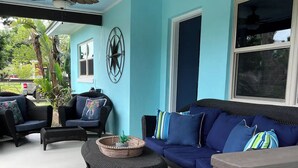Uma área de estar coberta ao ar livre com parede azul, duas ventoinhas no teto, móveis de vime e uma decoração de parede em formato de estrela.