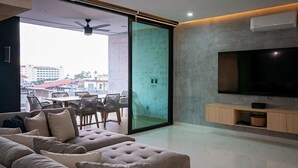 A modern living room with a large flat-screen TV, a sofa, and a dining area with chairs. - Vallarta Sunset Condo with Pool (Puerto Vallarta)