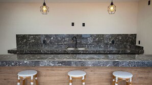 A kitchen with a marble countertop, a black faucet, and three wicker stools. - Vallarta Sunset Condo with Pool (Puerto Vallarta)