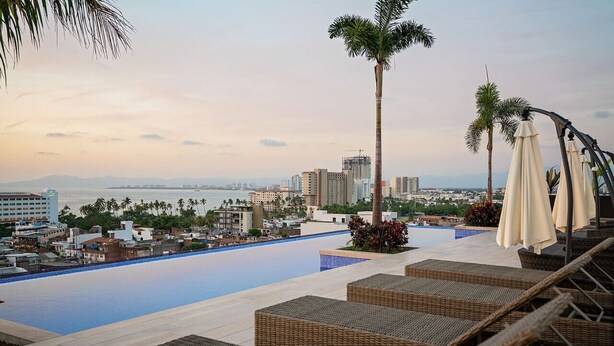 A rooftop pool area with lounge chairs and umbrellas, overlooking a cityscape and the sea. - Vallarta Sunset Condo with Pool (Puerto Vallarta)
