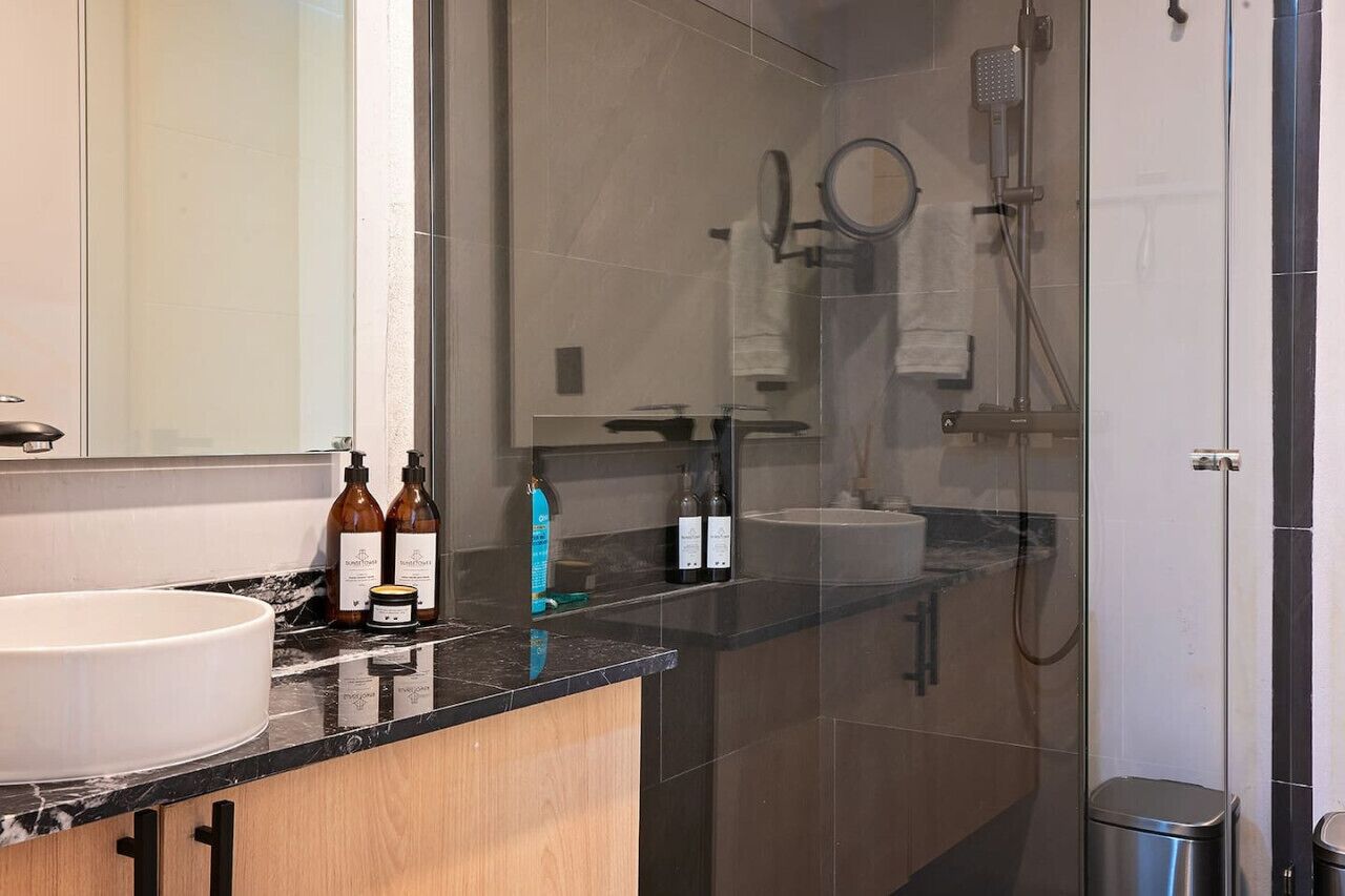 Un baño moderno con un espejo grande, un lavabo redondo y una zona de ducha con paredes de vidrio.