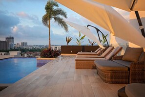 Un área de piscina en la azotea con sillones reclinables y vistas al horizonte de la ciudad.