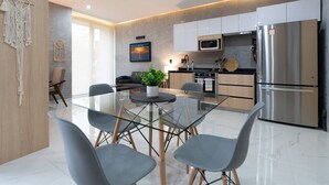 A modern kitchen with a dining area, featuring a glass table and chairs, a microwave, a refrigerator, and a sink. - Studio w/ Stunning Rooftop Pool (Puerto Vallarta)