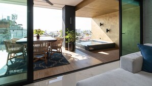 A modern living room with a glass wall, a dining area with wicker chairs, a ceiling fan, and a view of the cityscape. - Vallarta City View Condo w/ Pool (Puerto Vallarta)