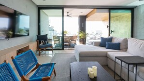 A modern living room with a sofa, chairs, a coffee table, and a TV mounted on the wall. - Vallarta City View Condo w/ Pool (Puerto Vallarta)