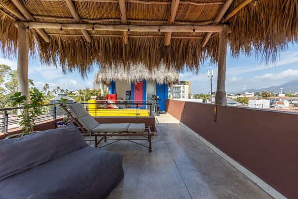 A rooftop terrace with a thatched roof, a pool, lounge chairs, and a view of the cityscape. - Trendy Beachside Apartment (Puerto Vallarta)