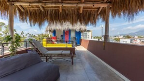 Um terraço no telhado com um telhado de palha, piscina, cadeiras de lounge e vista para a cidade.