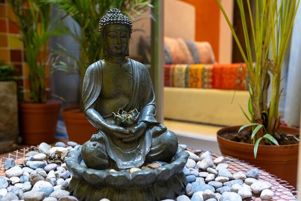Una estatua de Buda en posición sentada, con una flor de loto, rodeada de piedras y plantas en macetas.