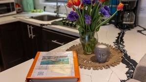 A kitchen counter with a vase of tulips and a candle, a placemat with a brochure, and a coffee maker.