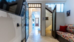 A hallway with a TV mounted on the wall, a sofa with a colorful cushion, and a staircase leading to another room.