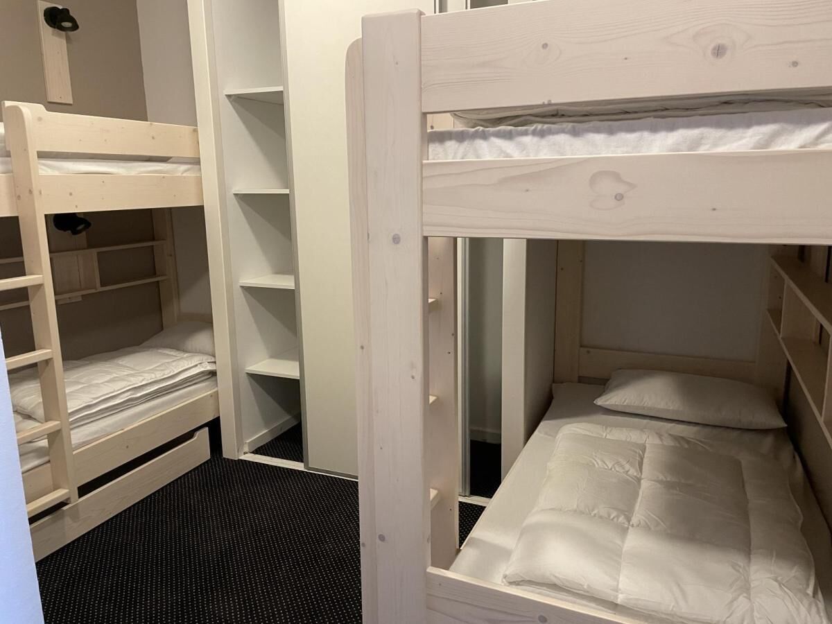 Un lit superposé avec des étagères de rangement, un bureau escamotable et un sol recouvert d’un tapis noir.