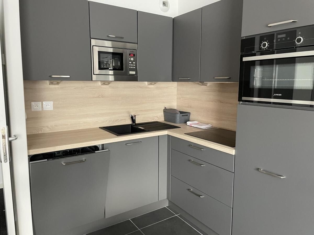 Une cuisine de taille réduite avec des meubles gris, un four à micro-ondes, un four traditionnel, un évier et un lave-vaisselle.