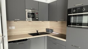 Une cuisine de taille réduite avec des meubles gris, un four à micro-ondes, un four traditionnel, un évier et un lave-vaisselle.