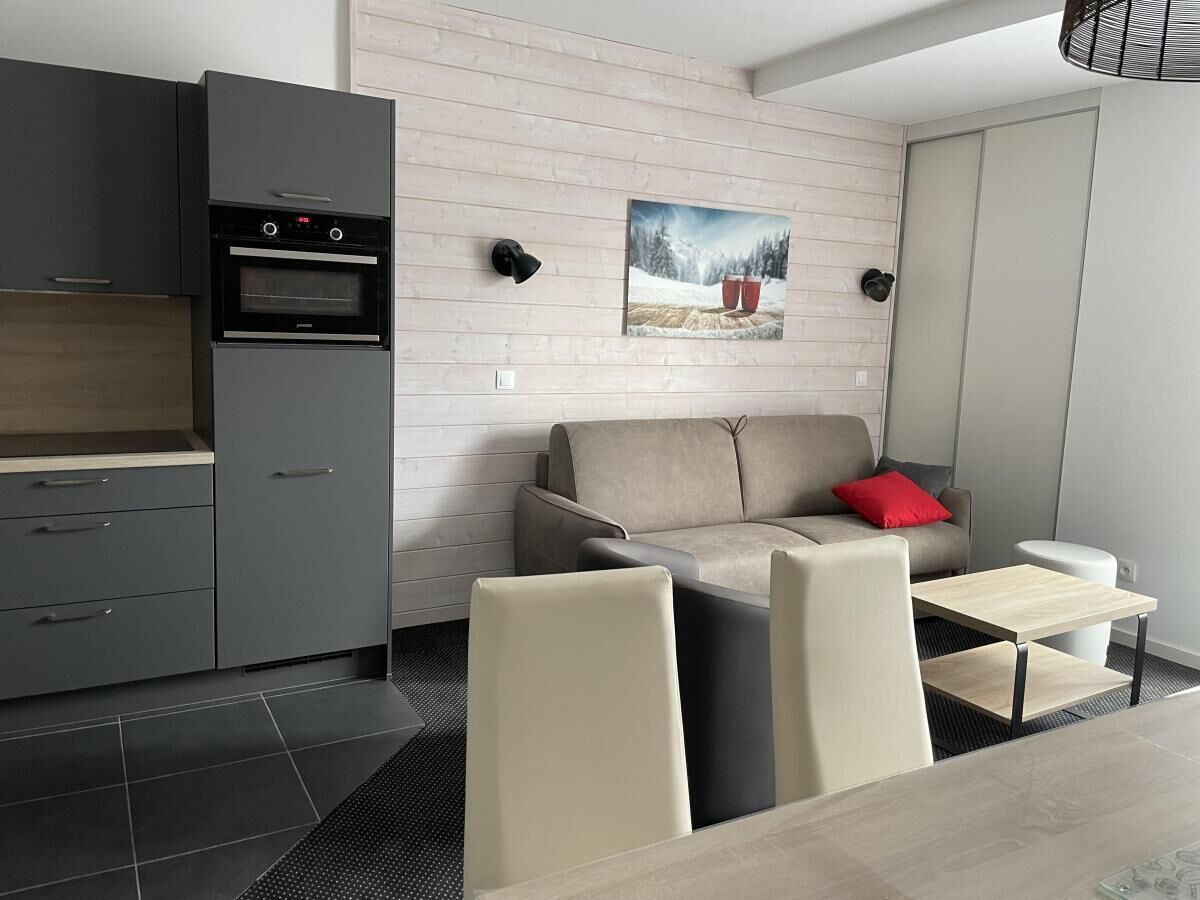 Une cuisine moderne avec des meubles gris, un four encastré et un coin repas comprenant un canapé et des chaises.