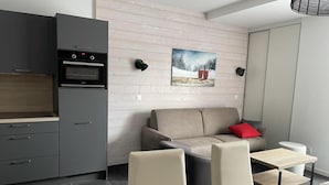Une cuisine moderne avec des meubles gris, un four encastré et un coin repas comprenant un canapé et des chaises.