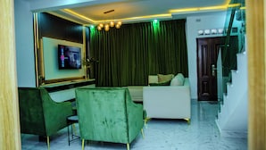 Una sala moderna con televisor de pantalla plana, sillones de terciopelo verde, un sofá blanco y una escalera.