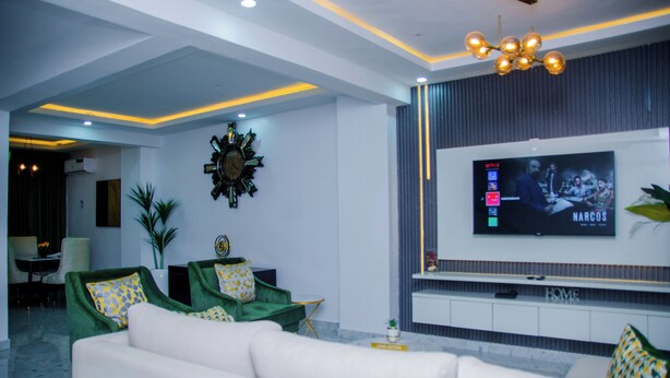 Una sala de estar moderna con un televisor de pantalla plana grande, sofás verde y blanco, y un reloj de pared decorativo.