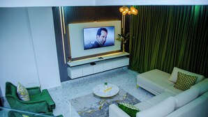 Una sala moderna con un televisor de pantalla plana montado en la pared, un sofá verde, un sofá blanco y un piso con estampado de mármol.