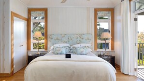 A bedroom with a large bed, two bedside tables with lamps, a ceiling fan, and a view through a window.