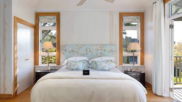 Un dormitorio con una cama grande, dos mesitas de noche con lámparas, un ventilador de techo y vistas a través de una ventana.