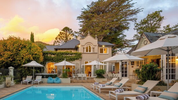 A pool area with lounge chairs and umbrellas, a large tree, and a building with a clock.