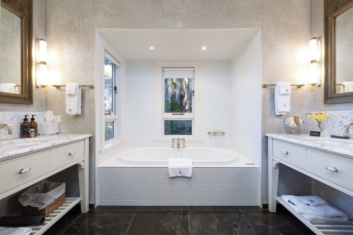 A modern bathroom with a large bathtub, two sinks, and a window with a view.
