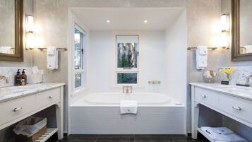 A modern bathroom with a large bathtub, two sinks, and a window with a view.