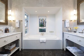 A modern bathroom with a large bathtub, two sinks, and a window with a view. - Pihopa Retreat (Nelson)