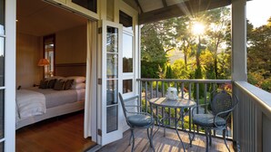 Une chambre avec une porte ouverte donnant sur un balcon équipé d’une table et de chaises, et offrant une vue sur des arbres et un bâtiment en arrière-plan.