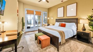 Une chambre à coucher comprenant un lit, des tables de chevet, un bureau, une chaise, un ventilateur de plafond et une fenêtre avec des stores.