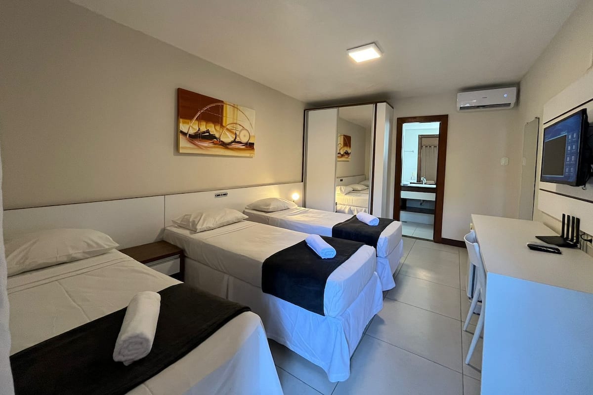 A hotel room with two single beds, a desk with a chair, a TV, and a painting on the wall.