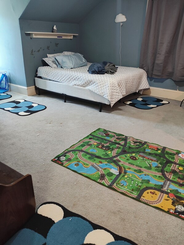 A bedroom with a bed, a blue and white patterned rug, a green Thomas the Train play mat, and a shelf with a small statue. - Spacious 7-bedroom house across from University and close to Downtown Lock Haven (Lock Haven)