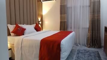 A hotel room with a bed, a red throw blanket, and a headboard with vertical lines.