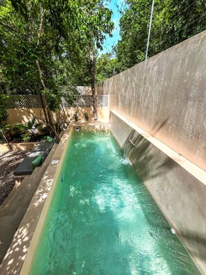 A narrow, rectangular pool with clear water, surrounded by a concrete wall and shaded by trees. - Oasis en la selva con piscina priva (Tulum)