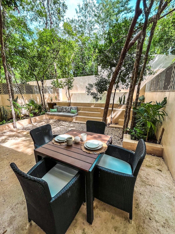 An outdoor dining area with a wooden table and wicker chairs, surrounded by greenery and a concrete wall. - Oasis en la selva con piscina priva (Tulum)