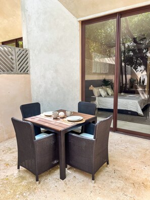 A dining area with a table and chairs, a sliding glass door leading to a bedroom, and a concrete floor. - Oasis en la selva con piscina priva (Tulum)