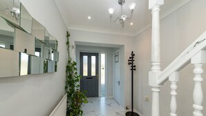 A hallway with a marble floor, a potted plant, a black floor lamp, and a white staircase with a balustrade.