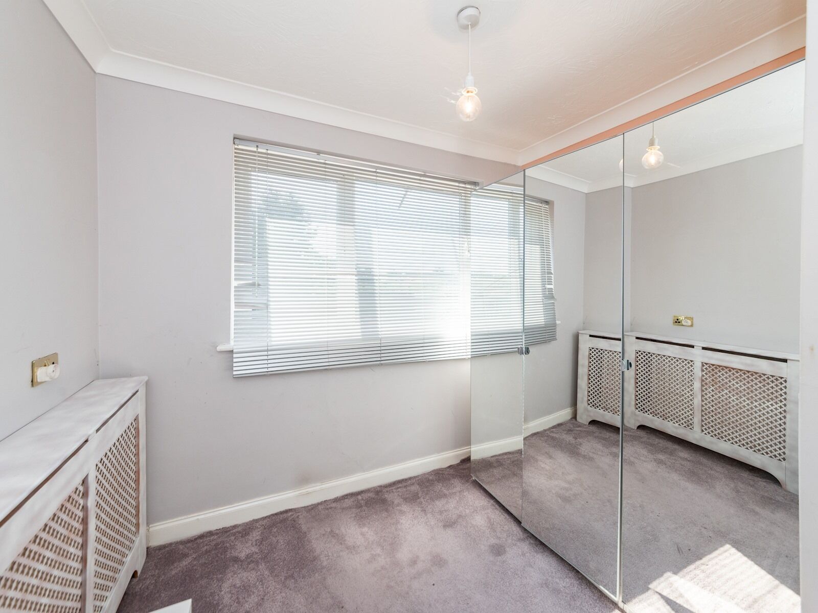 A room with a large window, a radiator, and a mirror on the wall.
