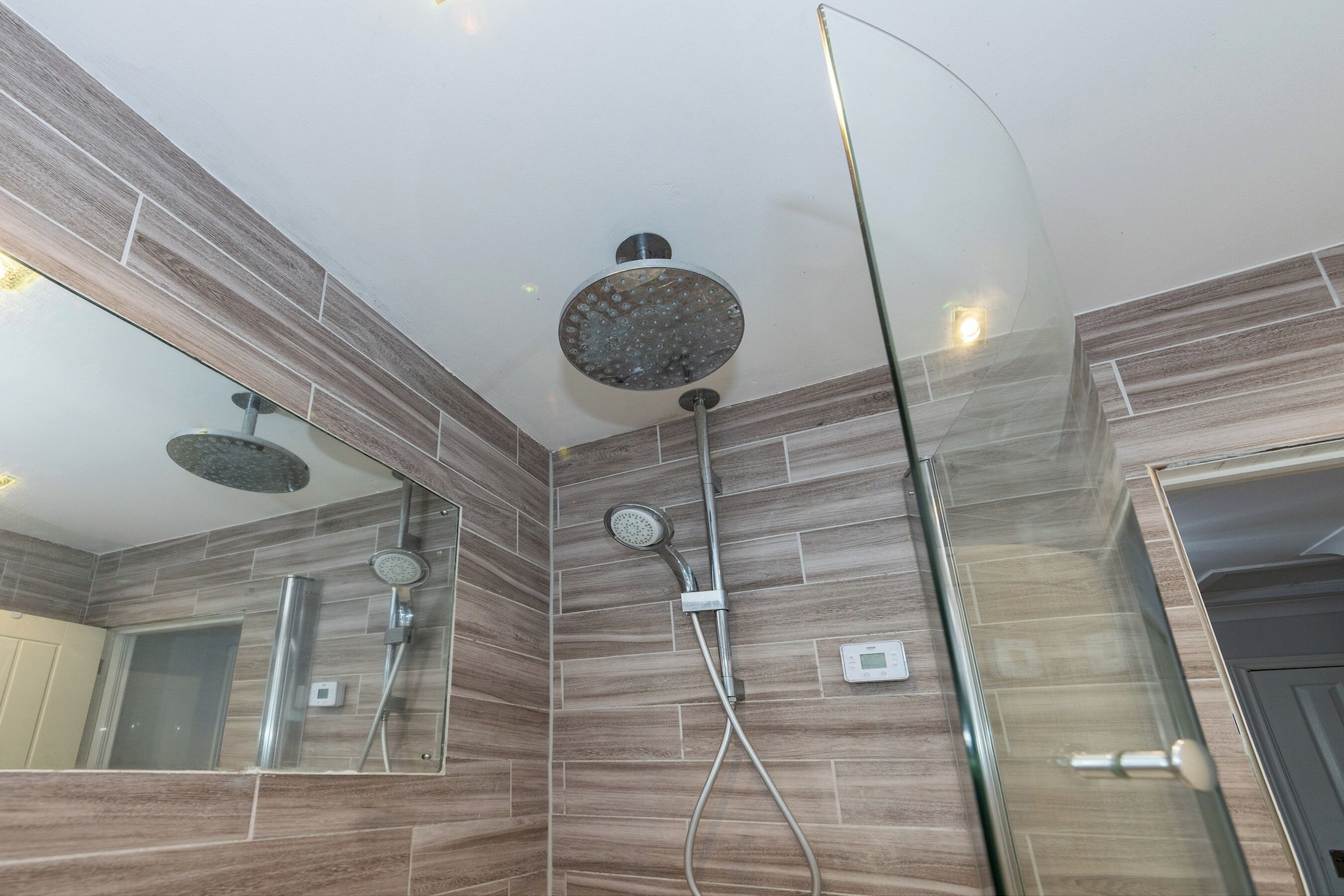 Un baño moderno con cabina de ducha de vidrio, un cabezal de ducha manual y un panel de control en la pared.