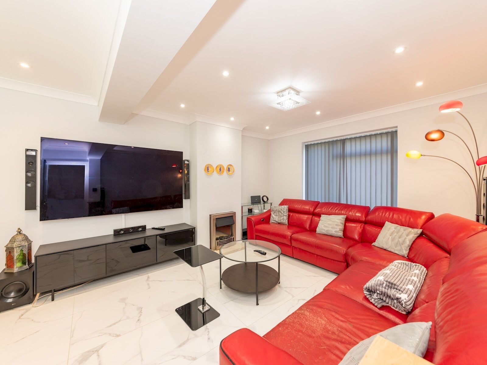 A modern living room with a large flat-screen TV, a red leather sofa, a coffee table, and a fireplace.