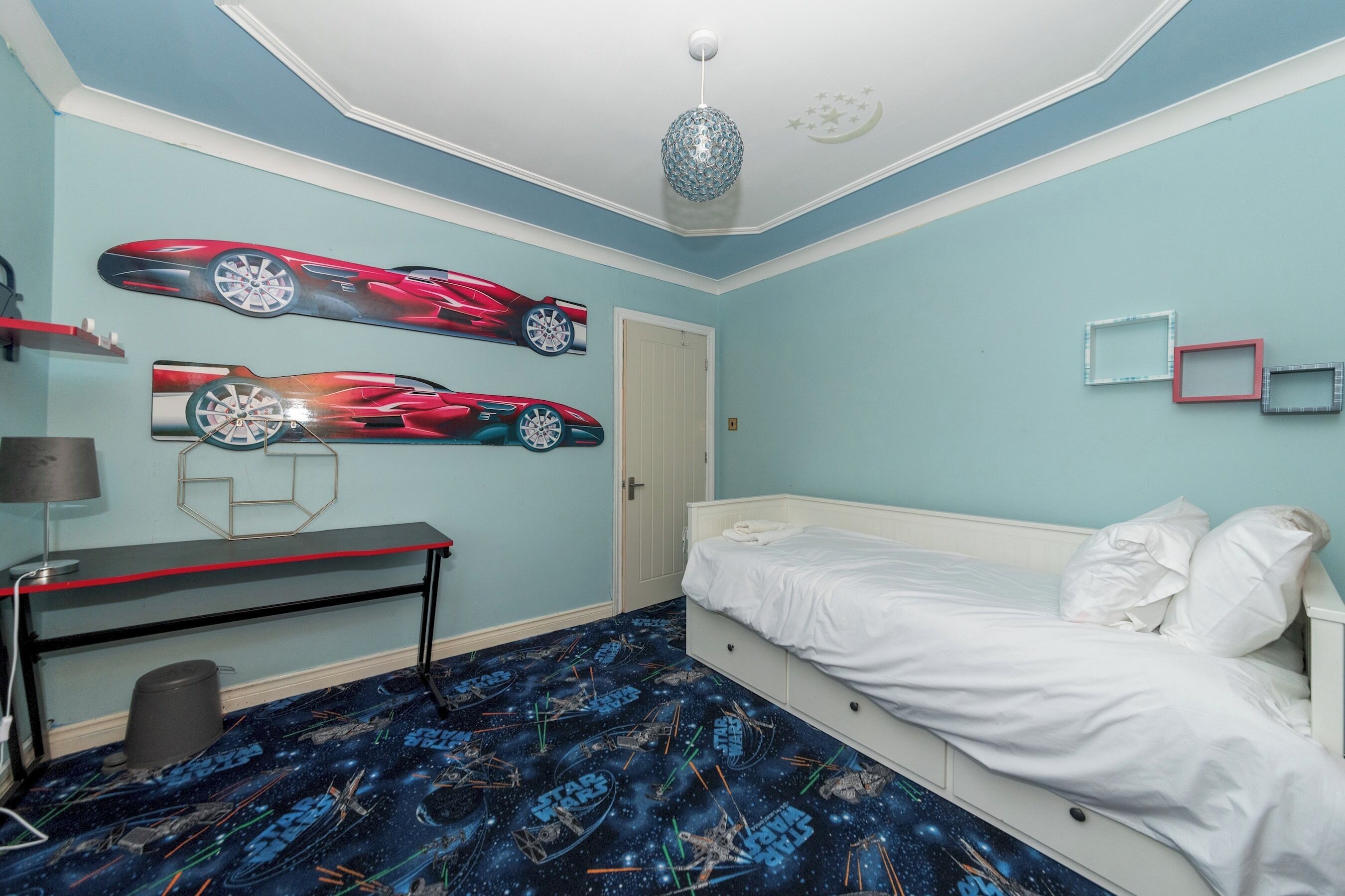 A bedroom with a bed, a desk, and wall art.