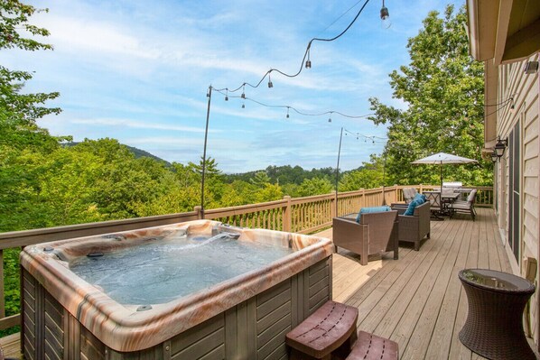 A deck with a hot tub, outdoor furniture, and a view of the forest.