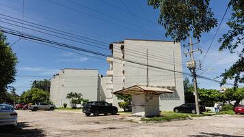 Un edificio con fachada plana, un pequeño quiosco de techo a dos aguas y coches aparcados en una calle adoquinada.